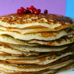 Pila di pancake senza farina, dorati e soffici, guarniti con bacche rosse.