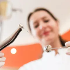 Dentystka z rękawiczkach trzyma wiertło i lusterko, gotowa do leczenia zęba.