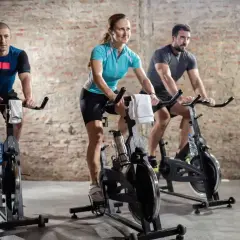 Trzy osoby ćwiczą na rowerach stacjonarnych. Intensywny trening spinningowy to świetny sposób na poprawę kondycji.