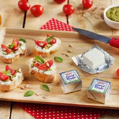 Bruschettas garnies de fromage frais, tomates et pesto, avec des emballages de Carré Frais le cendre et des tomates cerises sur un plateau en bois.