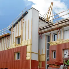 Chantier de construction : isolation extérieur bardage en cours, avec échafaudages et matériaux visibles.