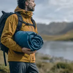Hombre con mochila y saco de dormir enrollado, listo para elegir su aventura.