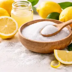 Cytryny i miska z białym proszkiem, przypominającym sól. Warto pamiętać o potencjalnej citric acid szkodliwość przy nadmiernym spożyciu.