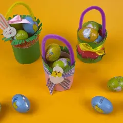 Tre cestini di Pasqua fai da te, decorati con coniglietti e pulcini, pieni di uova di cioccolato.