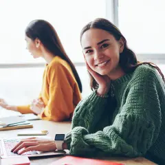 Junge Frau lächelt in die Kamera, während sie an ihrem Laptop sitzt. Sie ist Teil einer Gruppe, die sich mit dem Thema **Fernstudium Digitalisierung** beschäftigt.