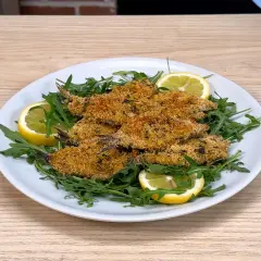 Piatto di alici al forno croccanti, servite su un letto di rucola fresca e guarnite con spicchi di limone.