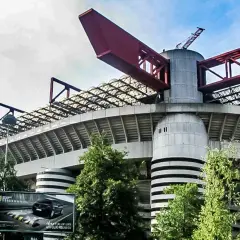 Charakterystyczny stadion Interu Mediolan z czerwonymi elementami konstrukcji i zielenią wokół.