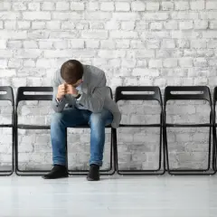 Zamyślony mężczyzna siedzi na krześle, zastanawiając się, czy na zasiłku dla bezrobotnych można dorobić.
