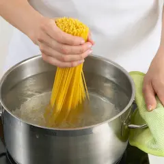 Hände halten Spaghetti, um sie in kochendes Wasser zu geben. Nudeln kochen ohne Herd ist hier nicht zu sehen, aber das Wasser brodelt.
