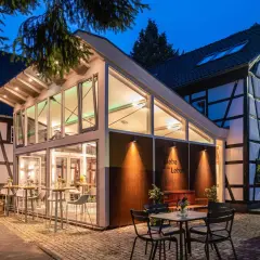 Abendstimmung an der buchmühle bergisch gladbach. Moderne Glasfront trifft auf Fachwerkhaus. Tische und Stühle laden zum Verweilen ein.
