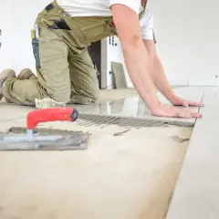 Pose d'un carrelage au sol, le carreleur ajuste la pose pour une épaisseur parfaite. Outils de pose à proximité.