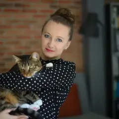 Kobieta w czarnej bluzce w kropki trzyma na rękach pręgowanego kota. To jej profilowe zdjęcie z kotem.