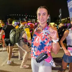Uśmiechnięta biegaczka po ukończeniu biegu na 100 km, trzymająca medal i bidon.