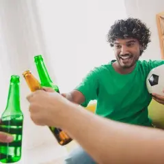 Un homme souriant avec un ballon de foot trinque avec des bières, une récompense parfaite après le sport.