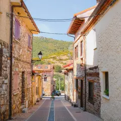 Calle empedrada en Puebla de la Sierra que ver. Casas de piedra y tejados rojos, con colinas verdes al fondo.