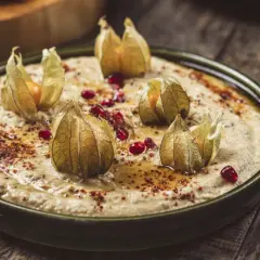 Krämig baba ganoush toppad med physalis och granatäppelkärnor på en rustik träyta.