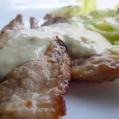 Tiernas lonchas de blanqueta de cerdo cubiertas con una cremosa salsa blanca, acompañadas de hojas verdes frescas.
