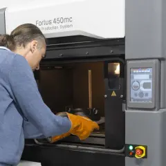 Mężczyzna w rękawicach zakłada element do drukarki 3D Fortus 450mc.