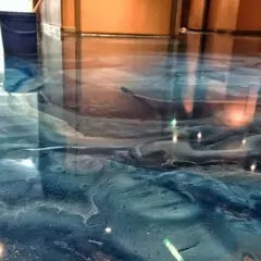 Błękitna żywica w garażu tworzy efekt fal oceanu. Widać niebieskie wiadro i odbicia światła.