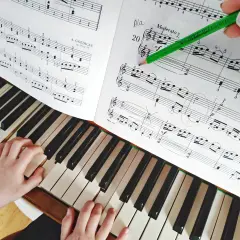 Dziecko ćwiczy lekcje gry na pianinie, śledząc nuty zielonym ołówkiem.