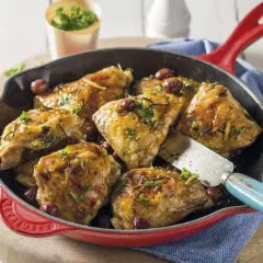Poêlée de cuisse de poulet dorée, garnie d'herbes et de quelques baies rouges, prête à être servie.