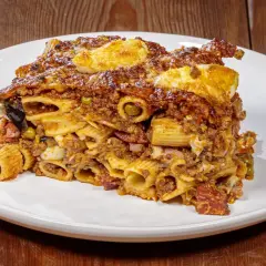 Porzione di pasta ncasciata ricca e saporita, con rigatoni, ragù, uova e verdure, servita su un piatto bianco.