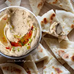 Ciotola di hummus di lenticchie con olio, paprika e prezzemolo, servito con pane pita tagliato a spicchi.