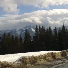 Śnieżne szczyty górskie, ciemny las świerkowy i chmury, które zdają się tańczyć na wietrze halnym.
