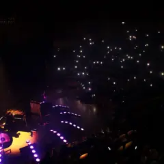 Koncert w ciemności: scena z muzykami, publiczność z zapalonymi telefonami.