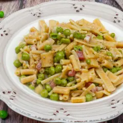 Un piatto di pasta con piselli, pancetta e pepe nero, servito su un piatto rustico.