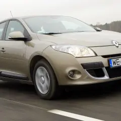 Złoty Megane 3 w ruchu drogowym, z widocznymi światłami i tablicą rejestracyjną WE 4130R.