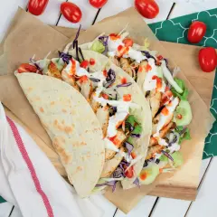 Kebab w tortilli z kurczakiem, warzywami i sosami, obok pomidorki.