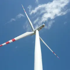 Biała mała elektrownia wiatrowa z czerwonymi pasami na łopatach obraca się na tle błękitnego nieba z chmurami.