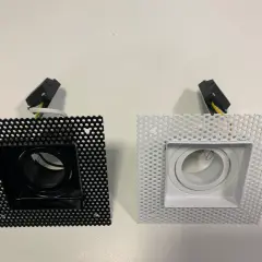 Dos focos empotrables cuadrados, uno negro y otro blanco, con rejilla perforada y conectores.