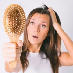 Mujer preocupada por la caída de pelo postparto, mostrando un cepillo con cabello.