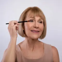 Mujer mayor aplicando sombra de ojos con brocha, aprendiendo como maquillar los ojos a partir de los 50 años para realzar su belleza natural.