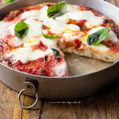 Pizza margherita appena sfornata in friggitrice ad aria, con mozzarella filante e basilico fresco su un tagliere di legno.
