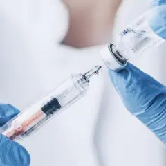 Ręce w niebieskich rękawiczkach pobierają płyn z fiolki do strzykawki. To może być propofol, środek znieczulający.