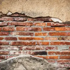 Stara, ceglana ściana z odpadającym tynkiem. Widać, jak wzmocnić ścianę z cegły, uzupełniając ubytki zaprawą.