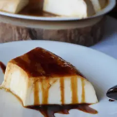 Un trozo de tarta de cuajada, cubierto de caramelo líquido, reposa en un plato blanco.