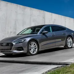 Elegancki, szary Audi A7 2025 z panoramicznym dachem stoi na tle betonowej ściany.