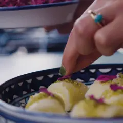 En hand dekorerar halawet el jibn med pistagenötter och rosenblad.