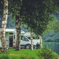 Kampery zaparkowane w malowniczej osadzie nad wodą, otoczone zielenią i drzewami.