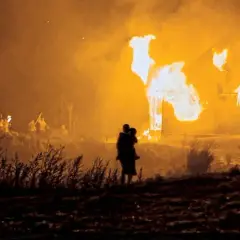 Płonące domy na Wołyniu. Sylwetka matki z dzieckiem na rękach obserwuje tragedię.