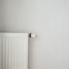 Radiateur blanc moderne, prêt à être alimenté par une pompe à chaleur. Un rideau discret complète la scène.