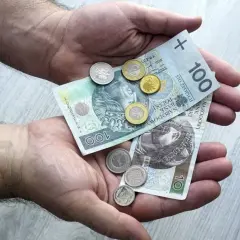 Dłonie trzymające polskie banknoty 100 zł i monety.
