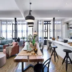 Un salón-comedor moderno con sofás azules y rosas, una mesa de madera rústica y **lámparas grises de techo** colgantes sobre la mesa.