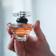 Dłoń trzyma flakonik perfum o bursztynowym kolorze, przypominający Baccarat Rouge.