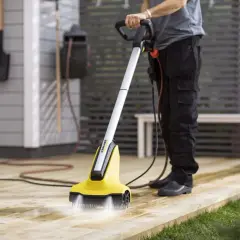 Person använder en borstmaskin för att slipa altanen. Vatten sprutar från borsten och rengör träet.