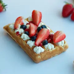 Gofry jak z budki, udekorowane bitą śmietaną, truskawkami, borówkami i granatem. Pyszny deser na białym tle.
